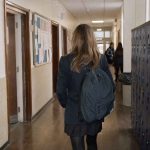 Anonymous schoolgirl walking through a British secondary school corridor with other pupils in the distance.