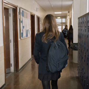 Anonymous schoolgirl walking through a British secondary school corridor with other pupils in the distance.